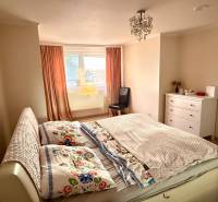 Hálószoba egy háromszobás lakásban, ággyal, szekrénnyel és narancssárga függönyös ablakkal.