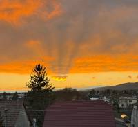 Boleráz naplementekor, láthatóak a házak tetejei és a drámai égbolt.