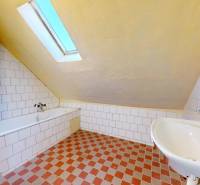 Családi ház fürdőszobája káddal, mosdóval és ferde mennyezettel.