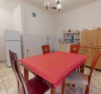 Családi ház konyhája fehér hűtőszekrénnyel, mikrohullámú sütővel és étkezőasztallal.