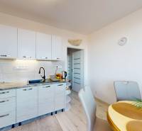 Konyha egy háromszobás lakásban, fa dekor padlóval, étkezőasztallal és fehér szekrényekkel.