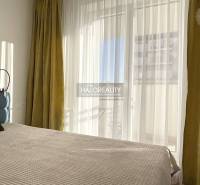 Világos hálószoba egy egyszobás lakásban nagy ablakkal és függönyökkel.