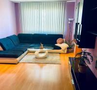 Nappali egy háromszobás lakásban kanapéval, dohányzóasztallal és fa dekorációjú padlóval.