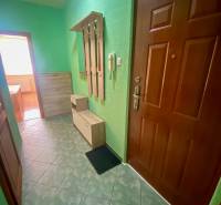 Folyosó zöld falakkal, csempével, fogassal és szekrényekkel egy háromszobás lakásban.