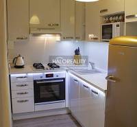 Konyha egy kétszobás lakásban fehér szekrényekkel és fa mintázatú padlóval.