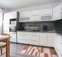 Konyha egy háromszobás lakásban fehér szekrényekkel és fa mintázatú padlóval.