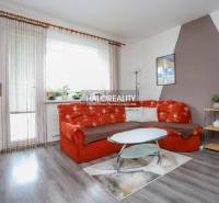 Nappali egy háromszobás lakásban narancssárga kanapéval és fa mintázatú padlóval.