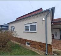 Családi ház Hurbanovóban világos homlokzattal és piros tetővel, bokrokkal körülvéve.