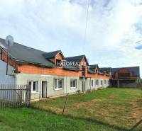 Üzlethelyiségek Tibaván, befejezetlen épület füves területtel és kerítéssel.