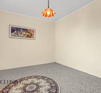 Szoba egy családi házban, szőnyeggel, függönnyel, képpel és csillárral a mennyezeten.