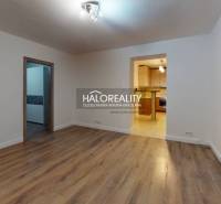 Nappali egy kétszobás lakásban, fa mintázatú padlóval és bejárattal a konyhába.