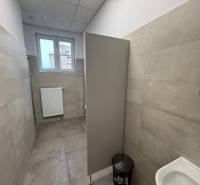 Irodák szürke burkolattal és WC-vel, kis ablakkal és bordás radiátorral.