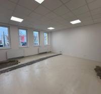 Üres irodák fehér falakkal, mennyezeti világítással és fa mintázatú padlóval.