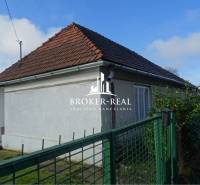 Fehér homlokzatú és ferde tetős családi ház Rudabányán, zöld kerítés mögött.