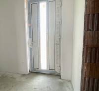 Családi ház bejárati ajtaja betonpadlóval és vakolatlan téglafallal.