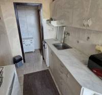 Konyha egy 3 szobás lakásban hosszú munkalappal és világos szekrényekkel.