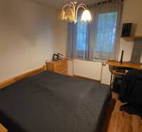 Hálószoba egy háromszobás lakásban ággyal, íróasztallal és fa dekorációjú padlóval.