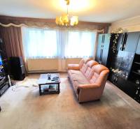 Nappali egy családi házban barna kanapéval, szekrényekkel és a falon lévő televízióval.