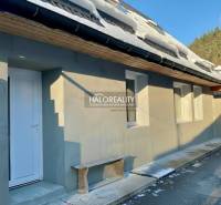 Családi ház Hroncban, hóval a tetőn, fehér ajtókkal és fa paddal.