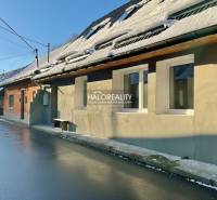 Családi ház Hroncban, hóval borított tetővel és nedves aszfaltúttal.