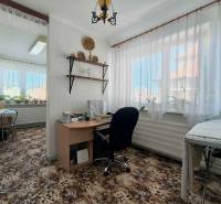 Szoba egy családi házban íróasztallal, növényekkel és virágmintás szőnyeggel.