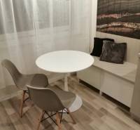 Étkező sarok kerek asztallal, két székkel és díszpárnákkal, fa dekorációjú padlóval.