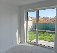 Családi ház belső tere nagy ablakkal a kertre, fehér falak és padló.