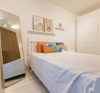 Hálószoba egy egyszobás lakásban ággyal, színes párnákkal, tükörrel és nagy szekrénnyel.