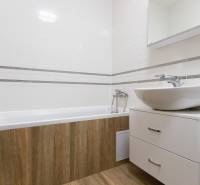 Fürdőszoba egy kétszobás lakásban káddal, mosdóval és fa dekoros padlóval.