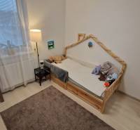 Gyerekszoba egy háromszobás lakásban, világos padlóval és könyvekkel teli polccal.