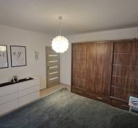 Hálószoba egy háromszobás lakásban, fa dekor padlóval, fehér bútorokkal, dekorációkkal a falakon.