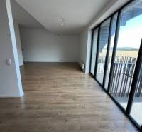 Világos nappali egy kétszobás lakásban, fa hatású padlóval és nagy ablakokkal.