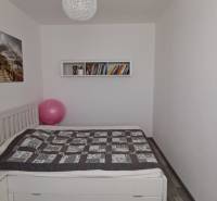 Hálószoba ággyal, képpel, könyvekkel és fa dekorációjú padlóval egy háromszobás lakásban.