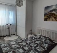 Hálószoba egy háromszobás lakásban ággyal, szekrénnyel és dekoratív fényképpel a falon.