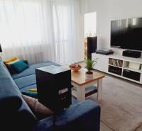 Nappali egy háromszobás lakásban kanapéval, televízióval és dohányzóasztallal.