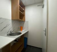 Kis konyha mosogatóval, polcokkal és narancssárga kancsóval az üzlethelyiségben.