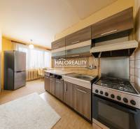 A háromszobás lakás konyhája sötét szekrényekkel, világos falakkal és nagy ablakkal.