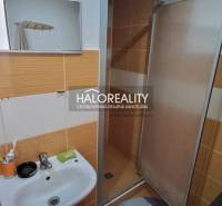 Fürdőszoba mosdóval és zuhanyzóval egy egyszobás lakásban, narancssárga-fehér csempékkel.