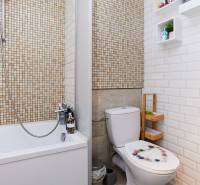 Fürdőszoba káddal, WC-vel, mozaikkal a falon és polcokkal a kiegészítők számára.