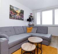 Nappali egy kétszobás lakásban sarokkanapéval, fa dekorációjú padlóval és ablakkal.