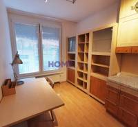 Dolgozószoba egy kétszobás lakásban, fa mintázatú padlóval, asztallal és könyvespolccal.