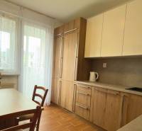 Konyha egy háromszobás lakásban fa dekorációval és világos bútorokkal, elegáns virágok az asztalon.