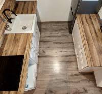 Konyha egy háromszobás lakásban fa dekorációjú padlóval és konyhaszekrényekkel.