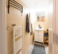 Fürdőszoba egy háromszobás lakásban világos csempékkel, mosdóval és létraszerű radiátorral.