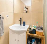 Fürdőszoba mosdóval, tárolóhellyel és világos csempével egy háromszobás lakásban.