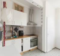 Konyha egy háromszobás lakásban, csempével, fehér szekrényekkel és fa dekorációjú pulttal.