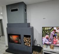 Családi ház belső tere kandallóval és fa dekorációjú padlón elhelyezett televízióval.