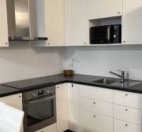 Konyha egy egyszobás lakásban fehér szekrényekkel, fekete munkalappal és fa mintázatú padlóval.