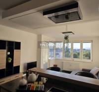 Nappali egy kétszobás lakásban világos falakkal és ablakokkal, bútorokkal berendezve.