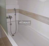 Két szobás lakás fürdőszobájában lévő kád kerámia burkolattal és zuhanyfejjel.